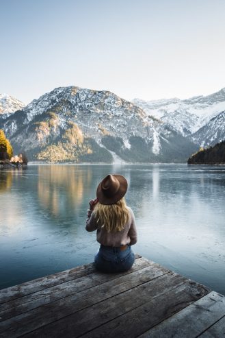 woman in brown jacket sitting on wooden dock near lake