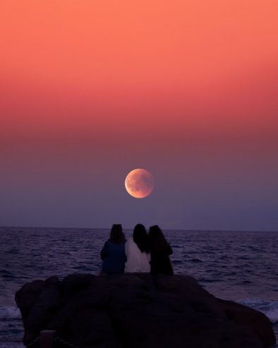 women sitting on a rock in front of the ocean 