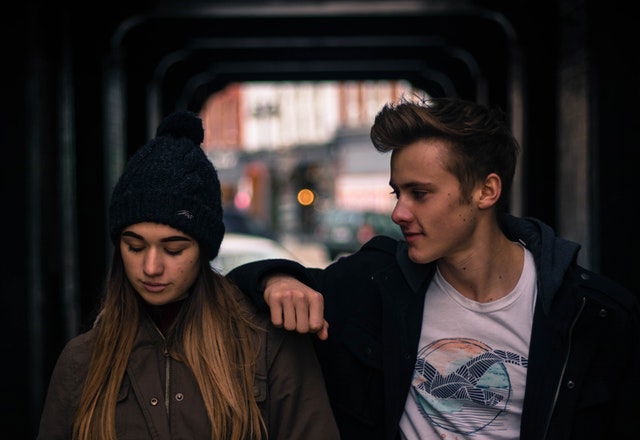 man talking to a woman with his right elbow on her left shoulder 