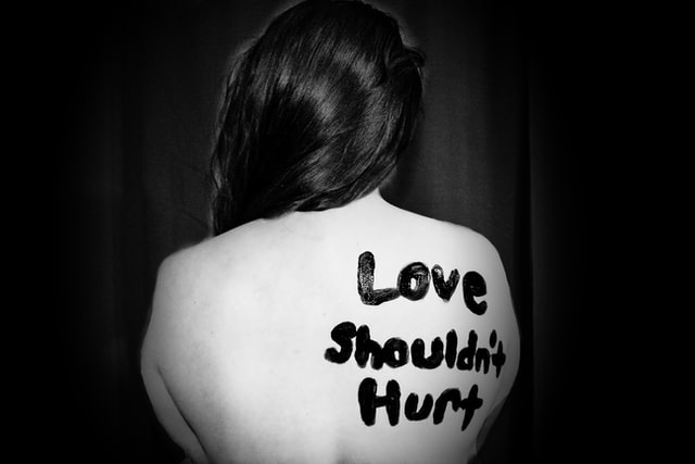 naked woman with the words " love shouldn't hurt" in her back 