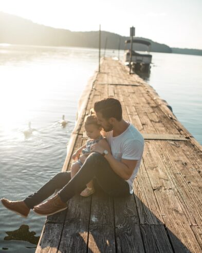 dad sitting on the pier of a lake with his daughter 