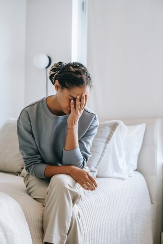 anxious black woman covering face with hand on bed 