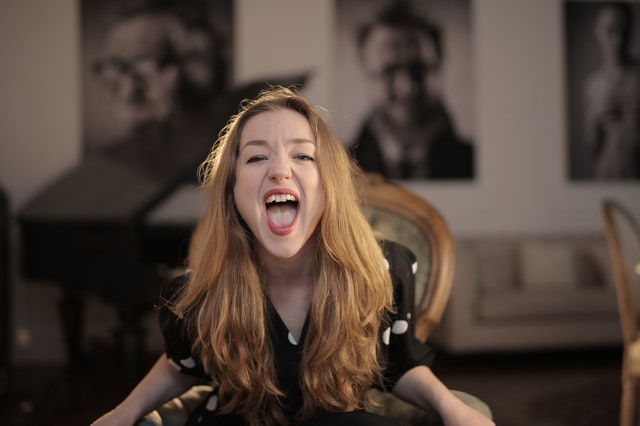 woman in black polka dots shirt sitting on chair shouting 