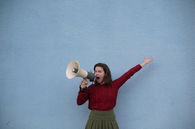 angry woman yelling into loudspeaker on blue background
