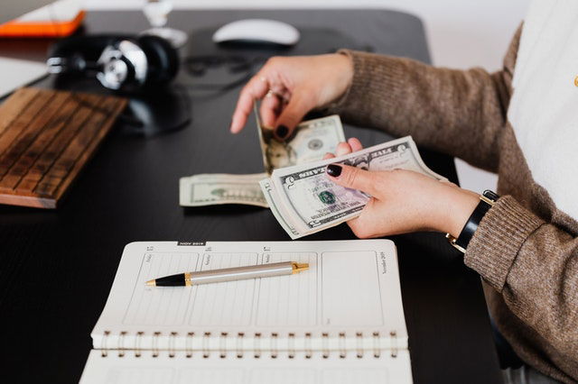 crop businesswoman counting money while sitting at desk