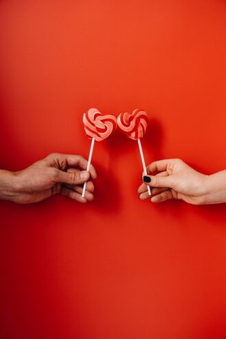 two hands holding heart shaped lollipops 